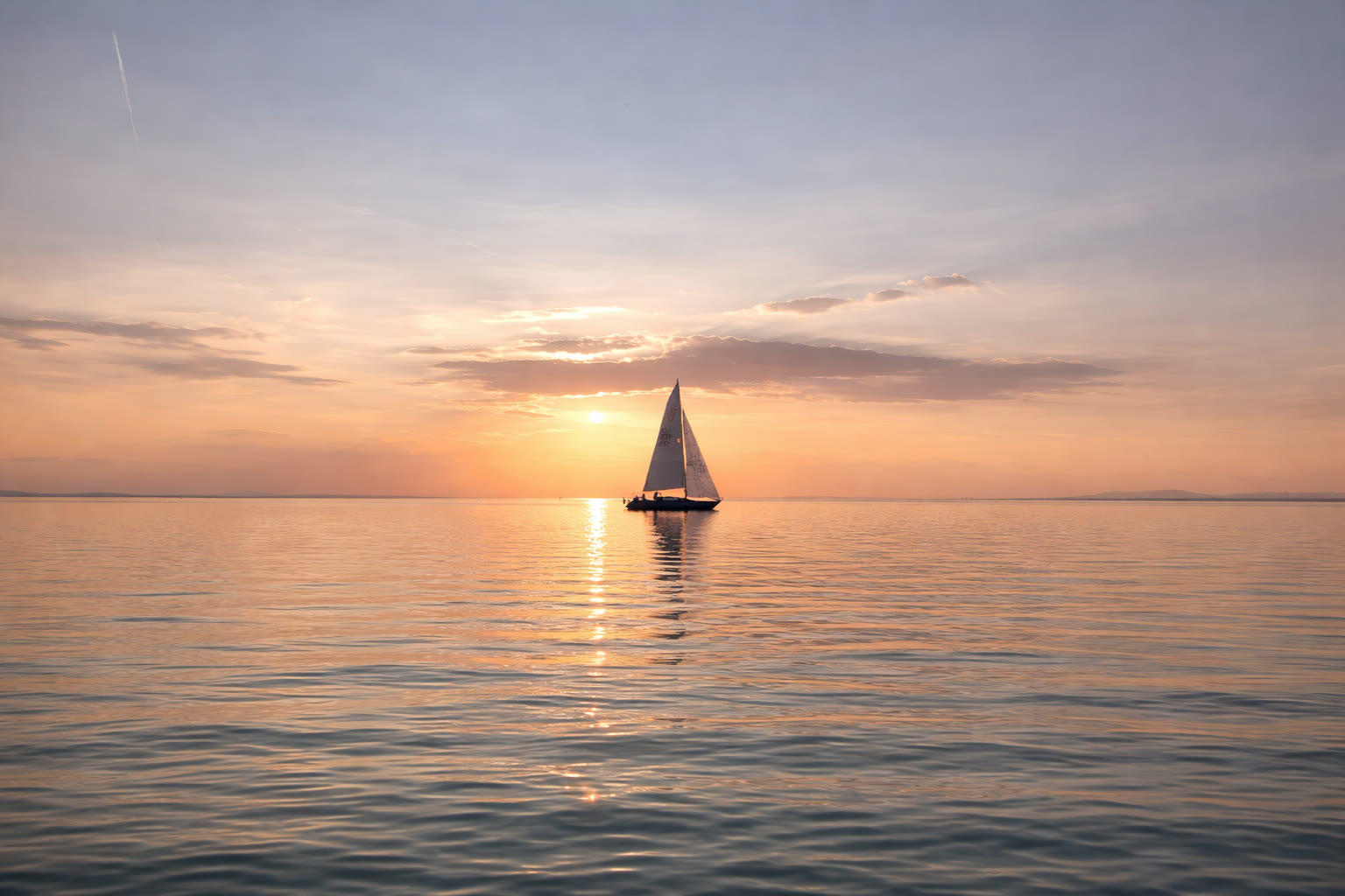 Segelboot bei goldenem Sonnenuntergang auf ruhigem Wasser